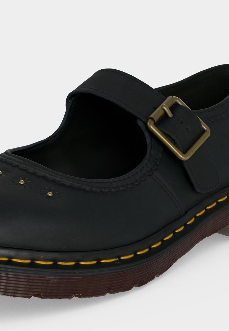 Scarpa Mary Jane nera con cuciture gialle, cinturino con fibbia in ottone e suola spessa marrone e strutturata.