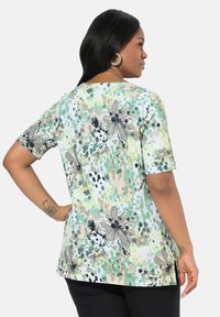 Topy s krátkým rukávem z měkké tkaniny, s zeleným květinovým vzorem a černými akcenty a volným střihem. Zaoblený lem a boční rozparky pro pohodlí.