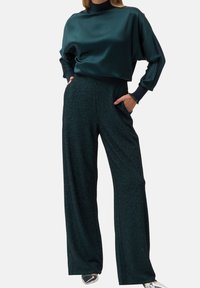 Top de satén color verde azulado oscuro con cuello alto y corte holgado, combinado con pantalones anchos y texturizados. Ambas prendas cuentan con bolsillos y detalles acanalados.