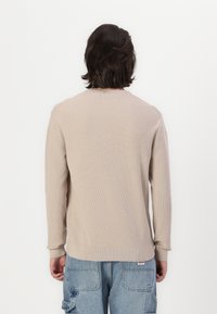 Maglione beige a maglia con scollatura tonda e maniche lunghe, caratterizzato da un motivo testurizzato e polsini a coste, indossato con pantaloni cargo blu.