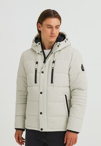 Quilted white puffer jacket with a hood, featuring black accents, adjustable drawstrings, and zippered side pockets. Soft texture.