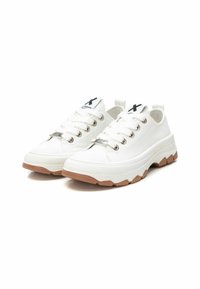 Zapatillas blancas de lona baja con parte superior de lona texturizada, suela de goma y ojales plateados. Incluyen una pestaña en el talón y una etiqueta con el logo en la lengüeta.