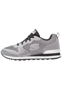 Grå sportskor med nätövre, svarta accenter, texturerade sidor och gummisula. Notabelt "S"-logotyp på sidan och snörning framtill.