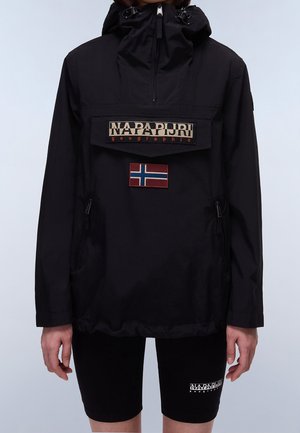 Persona con chaqueta negra con capucha con solapa frontal que dice "NAPAPIJRI geographic" y una parche con la bandera de Noruega, combinada con pantalones cortos negros.