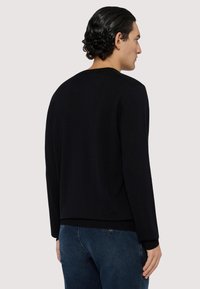 Svart stickad tröja med långa ärmar, rund halsringning och ribbade manschetter och nederkant. Slät textur; minimalistisk design utan synliga logotyper eller mönster.