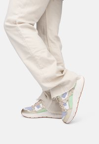 Sneaker multicolori con un mix di pannelli viola, verdi e beige, con una finitura metallica, lacci testurizzati e una suola bianca.