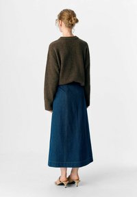 Brun strikket sweater med sænkede skuldre, parret med en lang blå denimnederdel med synlige stikninger og en lige kant.