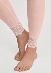 Blote voeten in roze geribbelde leggings met kantafwerking aan de enkels op een witte achtergrond.