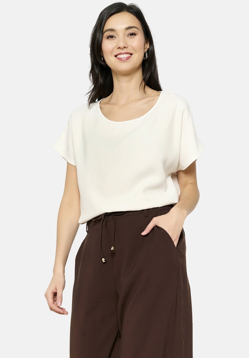 Top bianco a maniche corte con scollo rotondo abbinato a pantaloni larghi marroni con tasche laterali e vita regolabile con cordino.