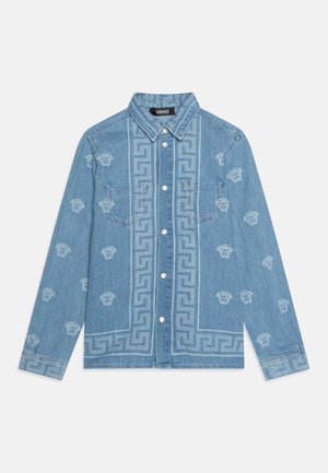 Jeanshemd aus hellblauem Stoff mit weißen gestickten Mustern und zwei Fronttaschen. Auffälliges griechisches Schlüsselmotiv entlang der Mitte.