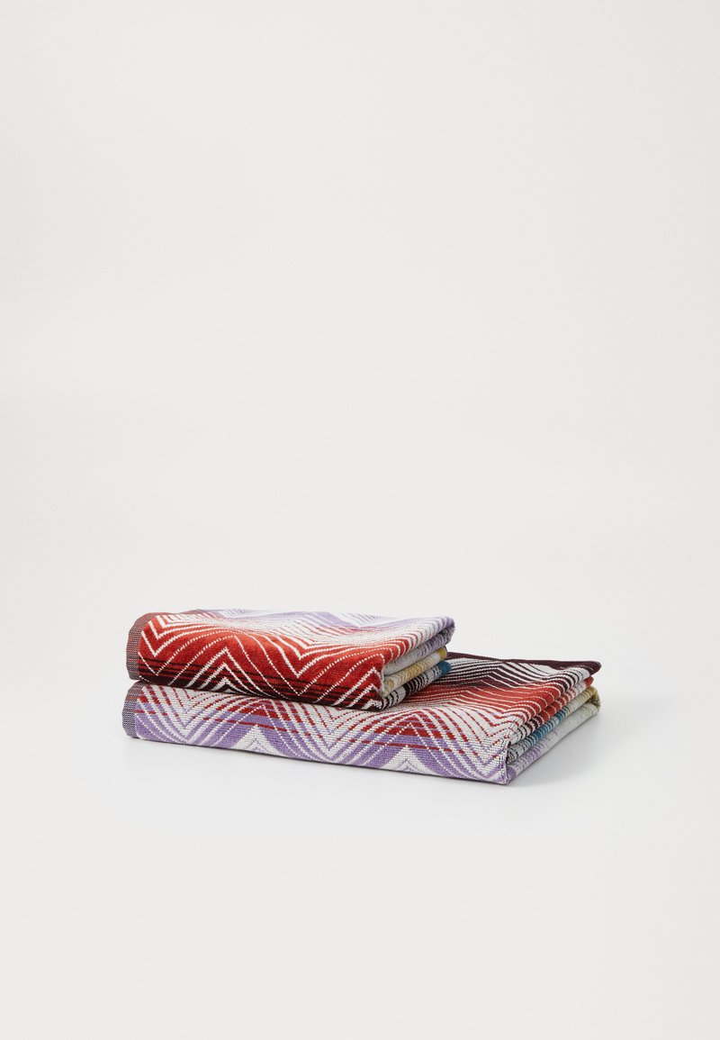 Twee opgevouwen handdoeken in rood en paars, met geometrische patronen. De textuur van de stof toont een mix van zigzag- en streepdesigns.