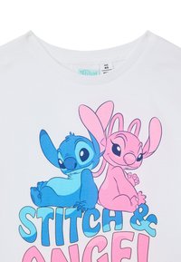 T-shirt in cotone bianco con il personaggio blu Stitch e il personaggio rosa Angel, con testo in grassetto che legge "STITCH & ANGEL!" in lettere colorate.