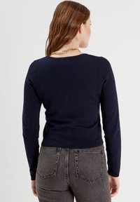 Suéter de lana azul marino de manga larga con cuello redondo, dobladillo acanalado y textura suave, combinado con jeans gris oscuro con bolsillos traseros.