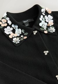 Black sweater with decorative floral appliqués in pastel colors and sequins. Features a collared neckline and shiny bead accents.