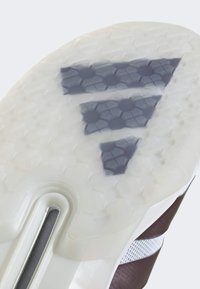 Gros plan de la semelle blanche translucide d'une sneaker avec un motif de semelle hexagonal noir et une partie de la tige marron et blanche.