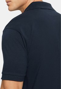 Polo shirt blu navy con un tessuto testurizzato, caratterizzato da un colletto classico e maniche corte. Design minimalista senza loghi o motivi visibili.