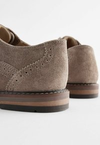 Bruine suède schoenen met een gladde afwerking, voorzien van decoratieve perforaties en een gelaagde houten zool met zwarte accenten.