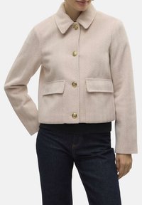 Veste herringbone rose courte avec col, ornée de boutons dorés, de deux poches avant et d'une bande inférieure noire ajustée.