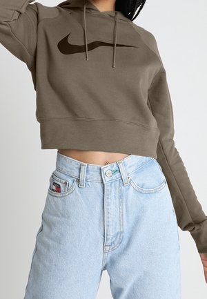 Person wearing a cropped olive green Nike hoodie and high-waisted light blue denim jeans with a visible Tommy Hilfiger logo on the pocket.