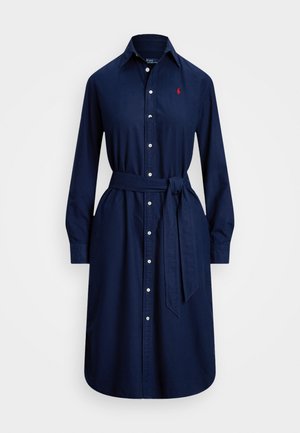 Mornarsko modra bombažna obleka s dolgimi rokavi, zapenjanjem na gumb, ovratnikom in zavezanim pasom. Ima majhen rdeč logotip na prsih.