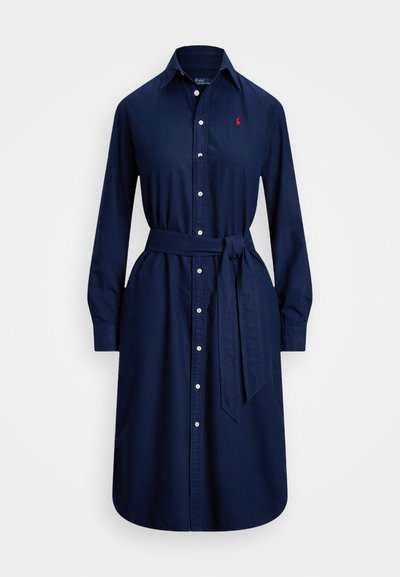 Vestuário em algodão azul marinho, tipo chemisier, com mangas longas, fecho de botões, gola e cinto amarrado na cintura. Apresenta um pequeno logótipo vermelho no peito.