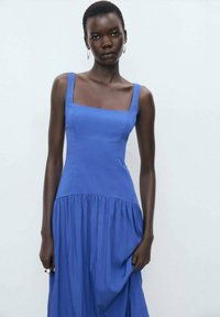 Blue dress with square neckline, fitted bodice, and flowy skirt. Made of lightweight fabric, features subtle pleating at the hem.