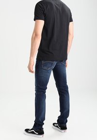 Mörkblå jeans i slim fit med bakfickor och kontrasterande sömmar. Bärs med en svart t-shirt och svarta sneakers.