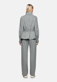 Grauer Nadelstreifenanzug mit tailliertem Sakko mit langen Ärmeln und passenden weiten Hosen. Weicher Stoff mit glatter Textur.