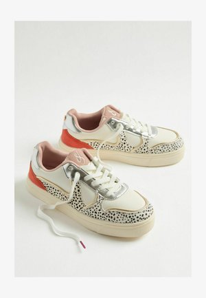 Weiße Sneakers mit schwarzem gepunktetem Muster, silbernen Akzenten und orangefarbener Ferse. Sie haben ein pinkes Innenfutter und weiße Schnürsenkel mit lila Spitze.