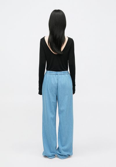 Melna garām piedurknēm blūze ar zemu muguru, kas apvienota ar brīvām, gaiši zila džinsām, kas aprīkotas ar elastīgu jostasvietu. Vienkāršs, mājīgs piegriezums.