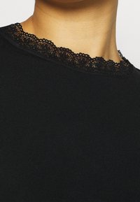 Svart tröja med rund halsringning prydd med delikat svart spetskant. Tyget verkar mjukt med en slät textur.