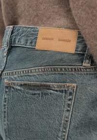 Tuvo plāns ar zilo džinsu aizmugures kabatu, kurā ir iedegts brūns ādas zīmola etikete, kas piestrādāta pie jostas, pārī ar brūnu pūkainu džemperi.