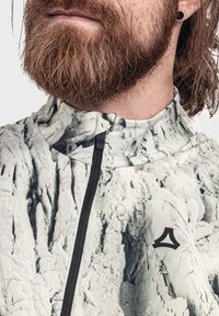 Leichte Zip-Jacke mit einem strukturierten weißen und grauen Marmor-Muster, hohem Kragen und einem kleinen schwarzen Logo auf der Brust.