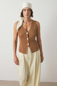 Brun ribbet tanktop med V-hals og fem dekorative knapper, parret med løse cremefarvede bukser og et hvidt tørklæde.