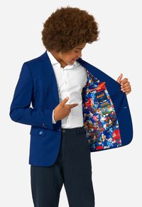 Jūras zila bleizeris ar divām pogām un krūšu kabatu, ar krāsainu kartūnas rakstu odere, kurā attēloti varoņi no Sonic the Hedgehog.