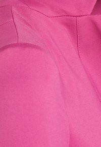 Detail růžové tkaniny s hladkou strukturou a viditelnými zakřivenými i rovnými švy.