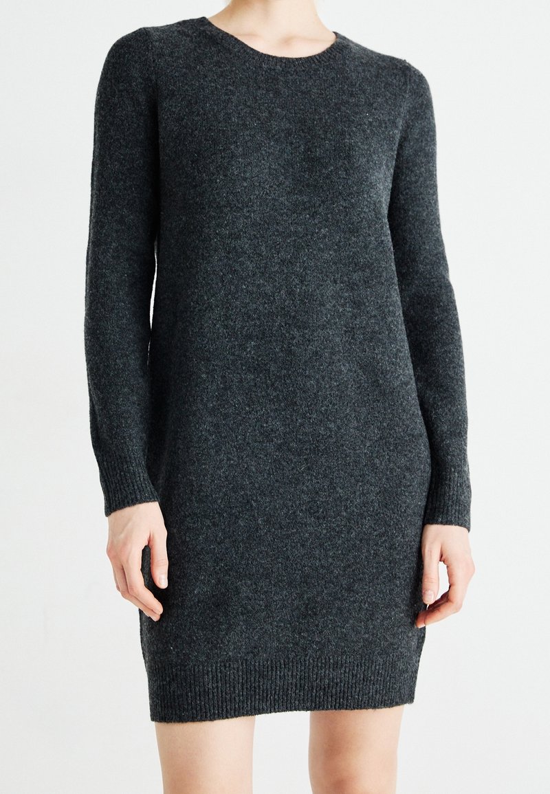 Robe en maille gris foncé à manches longues avec col rond, poignets et ourlet côtelés, portée par une personne debout sur un fond clair uni.