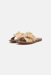 Sandales tissées beiges avec deux bandes croisées, dotées d'une boucle décorative dorée et d'une semelle brune texturée.