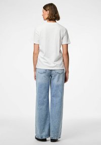 Camiseta de algodón blanca de manga corta, combinada con unos vaqueros de pierna ancha de color azul claro, con una textura gastada y bolsillos traseros.