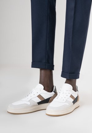 Baskets blanches et beiges avec des accents en daim texturé et en cuir, présentant une semelle épaisse et un design qui combine des éléments sportifs et décontractés.