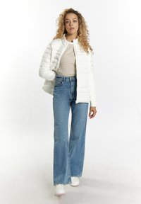 Hvid, quilted pufferjakke med høj krave, parret med lyseblå brede jeans og hvide sneakers. Ingen synlige grafikker eller mønstre.