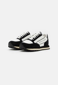 Czarno-białe sneakersy wykonane z zamszu i materiałów tekstylnych, z białą podeszwą i sznurówkami oraz detalem logo z boku.