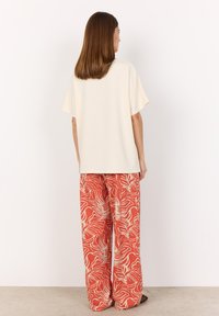 Loose cream top with short sleeves paired with wide red pants featuring a white wavy pattern. Simple design with a relaxed fit.