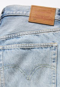 Poche arrière d'un jean en denim bleu clair avec couture jaune et une étiquette en cuir marron Levi Strauss au-dessus de la poche.