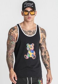 Čierny tielko s bielym lemovaním, ktoré zobrazuje farebnú grafiku medvedíka. Tkanina sa zdá hladká; dizajn je umiestnený na hrudi.