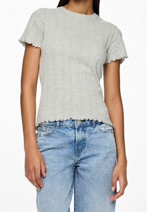Mujer que lleva un top de punto acanalado de manga corta en gris claro con bordes festoneados combinado con vaqueros de mezclilla azul claro de talle alto.
