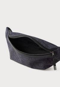 Mørkegrå mønstret hofteveske med �åpen sølvglidelås og svart stoffinteriør på hvit bakgrunn.