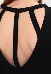 Black top featuring a V-back design with three contrasting vertical straps. Soft texture highlights the garment's casual style and fit.