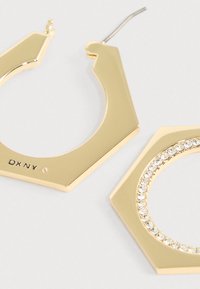 Kulla tooniga kuusnurkse kujuga rõngakujulised kõrvarõngad, millel on sile viimistlus, kristallidega kaunistatud äär ja konkskinnitus. Märgistatud "DKNY".