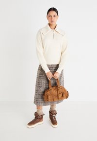 Suéter de punto color crema con cuello grande, falda de cuadros, bolso de pana marrón y botas aislantes marrones con suelas y cordones blancos.